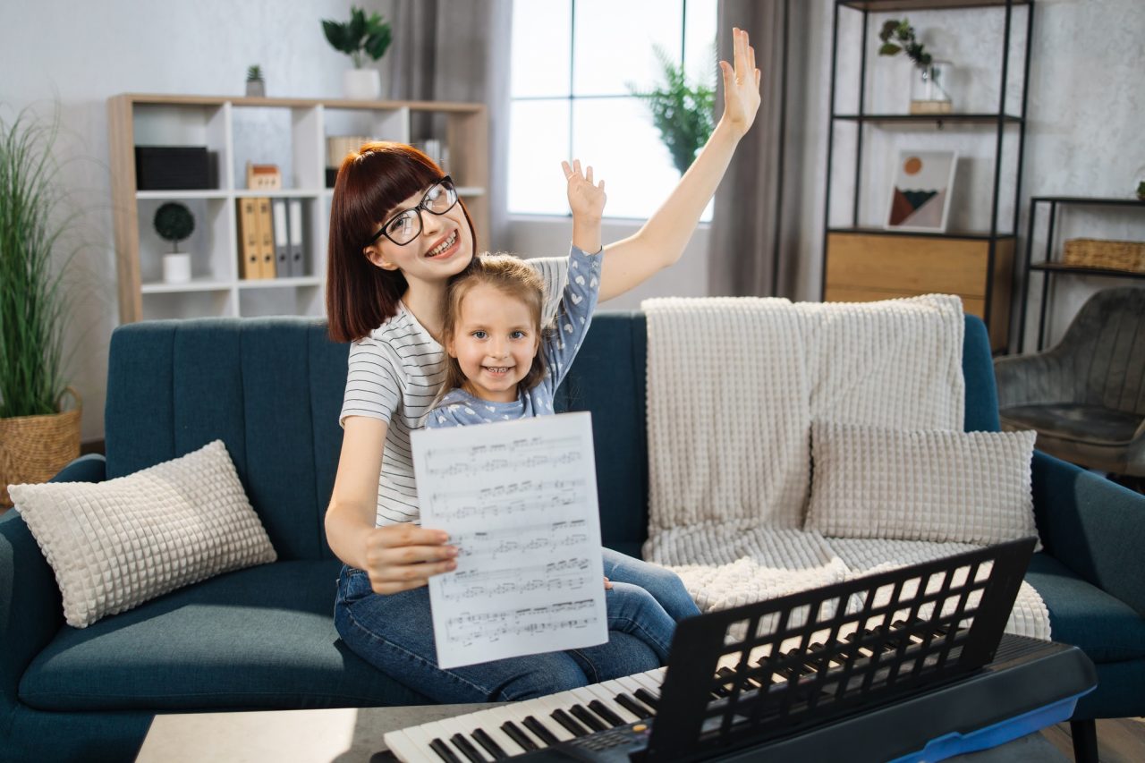 Mother teaching playing piano using notes her daughter.