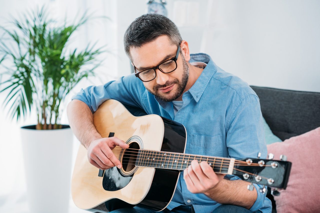 portrait of man in eyeglasses playing acoustic guitar at home